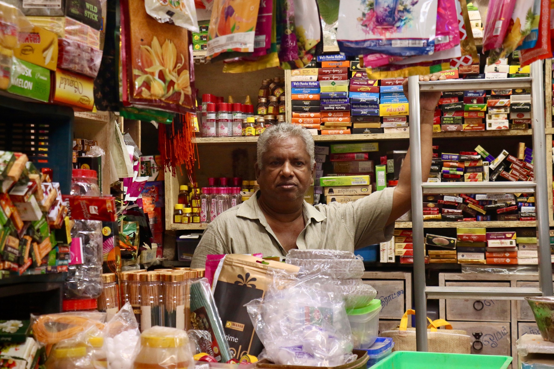 A male shopkeeper behind the counter of a neighbourhood store — illustrative photograph